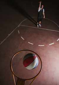 From above determined basketball player in sportswear performing skillful foul shot from standing position while training alone on brown sport field