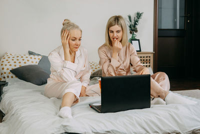 Blonde women at home watching a movie on a laptop and eating popcorn. the concept of friendship. 