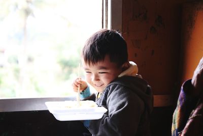 Smiling boy eating food by window