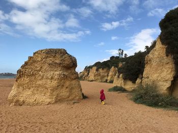 Girl walking by rock formations against sky at beach