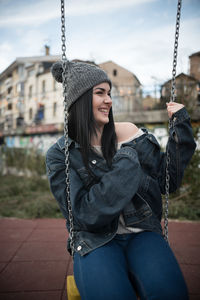 Young woman wearing denim jacket sitting on swing at playground