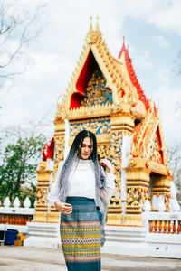 Portrait of smiling young woman outside temple against building