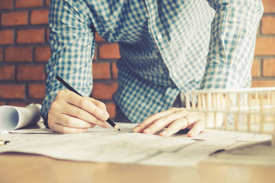 Midsection of man drawing on blueprint at desk