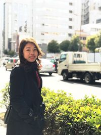 Portrait of smiling young woman standing on street in city