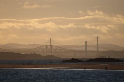 Suspension bridge over sea against cloudy sky