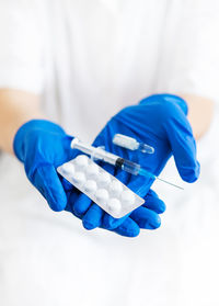 A young doctor holds a vaccine, syringe and pills in latex blue gloves. 