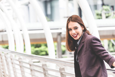 Portrait of smiling young businesswoman standing on elevated walkway 