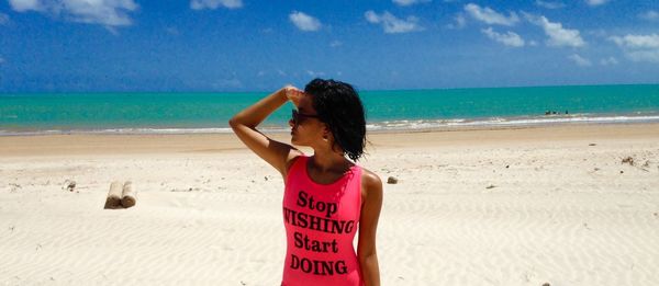 Woman wearing pink tank top with text at beach against sky during sunny day