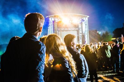 Rear view of people enjoying music concert against sky at night