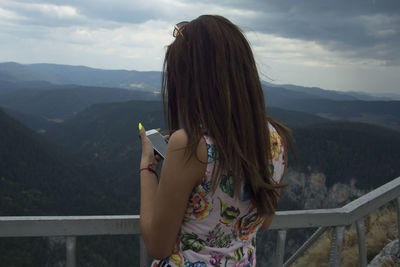 Rear view of woman using mobile phone while standing against mountains