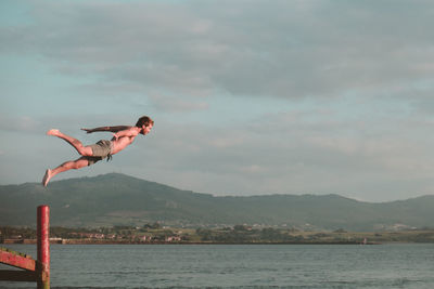 Man jumping over sea against mountains