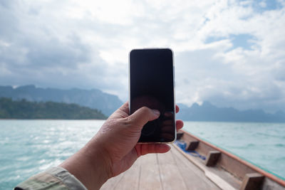 Midsection of person holding mobile phone against sky