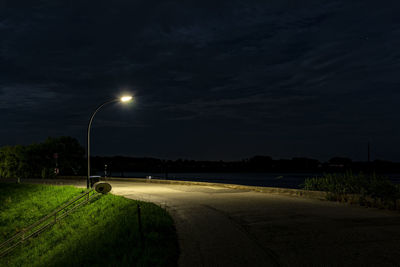 Illuminated street lights by road against sky at night