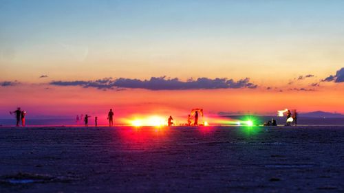 Silhouette people on beach against sky during sunset