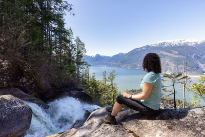 Side view of young woman sitting on rock