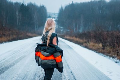 Rear view of woman removing jacket while standing on snow covered road