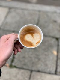 Cropped hand holding coffee cup over footpath