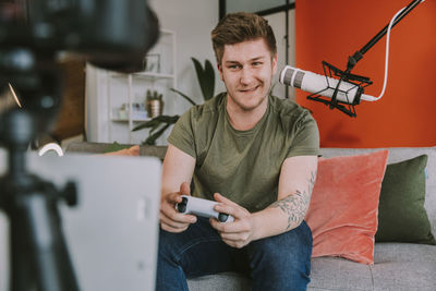 Portrait of smiling young man using mobile phone while sitting on sofa