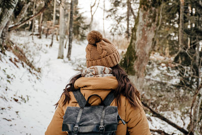 Rear view of woman in winter clothes hiking in nature. forest, snow, exploring, backpack.