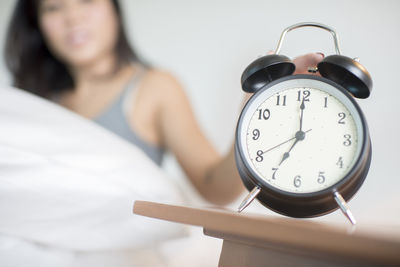 Woman closing alarm clock while sitting on bed at home