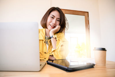 Portrait of smiling young woman using phone on table