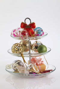 Close-up of multi colored christmas decorations in cake stand against white background