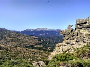 Scenic view of rocky mountains against clear blue sky with flying vultures