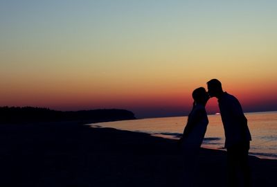 Silhouette women on beach against sky during sunset