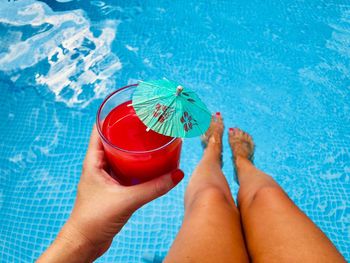 Low section of woman holding drink glass at swimming pool