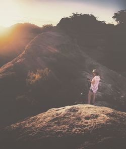 Rear view of woman standing on cliff against sky