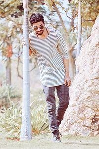 Portrait of young man wearing sunglasses standing on tree trunk