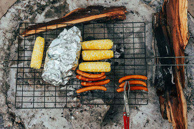 Dinner on camping grill with corn, hot dogs, sausages, and tin foil dinner.