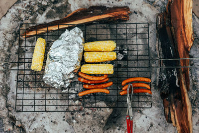 Dinner on camping grill with corn, hot dogs, sausages, and tin foil dinner.