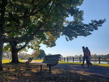 Rear view of man and woman walking on footpath by lake in park