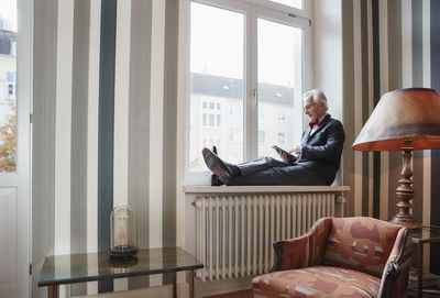 Senior man sitting in windowsill using tablet