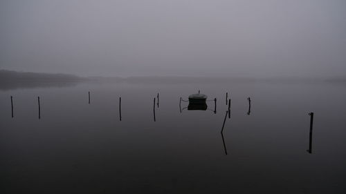 Wooden posts in lake against sky