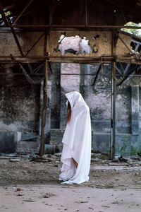 Woman wearing white textile standing against old abandoned building
