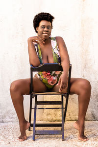 Portrait of woman sitting on chair against wall