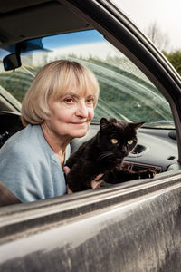 Senior adult woman holding black cat sitting in car driving to europe forced to flee from ukraine