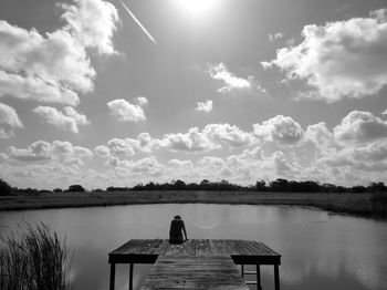 Person sitting on pier over lake against sky