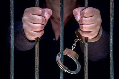 Midsection of prisoner standing behind bars