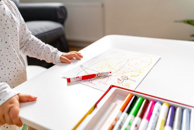 Girl with felt tip pens drawing at table in living room
