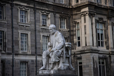 Close-up of monument at campus of trinity colege in dublin with historic facade in background