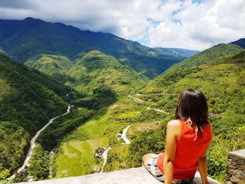 Rear view of woman looking at mountains against cloudy sky