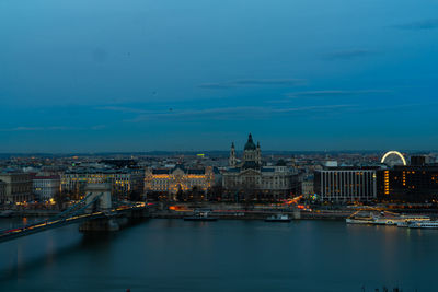 Illuminated buildings by river against sky at night