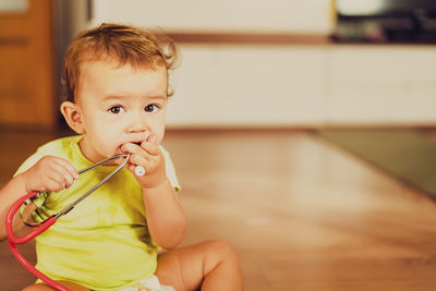 Portrait of cute baby girl biting stethoscope while sitting at home