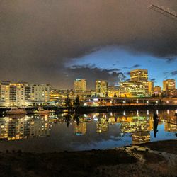 Illuminated cityscape by sea against sky at night