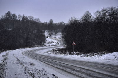 Snow covered road amidst trees against sky