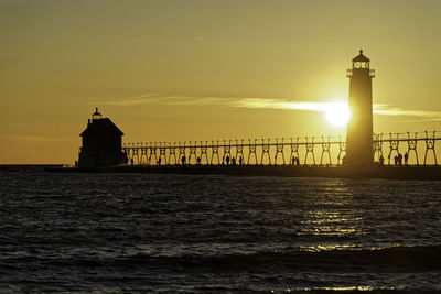 Lighthouse by sea against sky during sunset