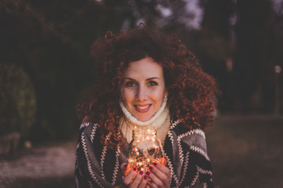 Portrait of young woman holding illuminated string lights in jar